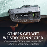 Cardo Packtalk device on a car dashboard with water droplets, emphasizing waterproof certification.